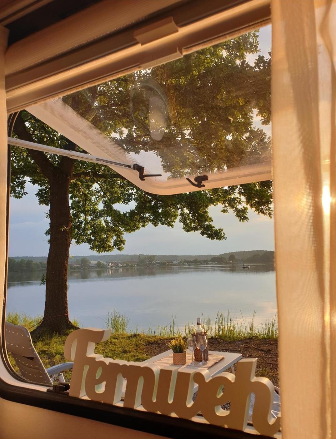 Blick aus einem Wohnwagen-Fenster zum See mit Deko Fernweh